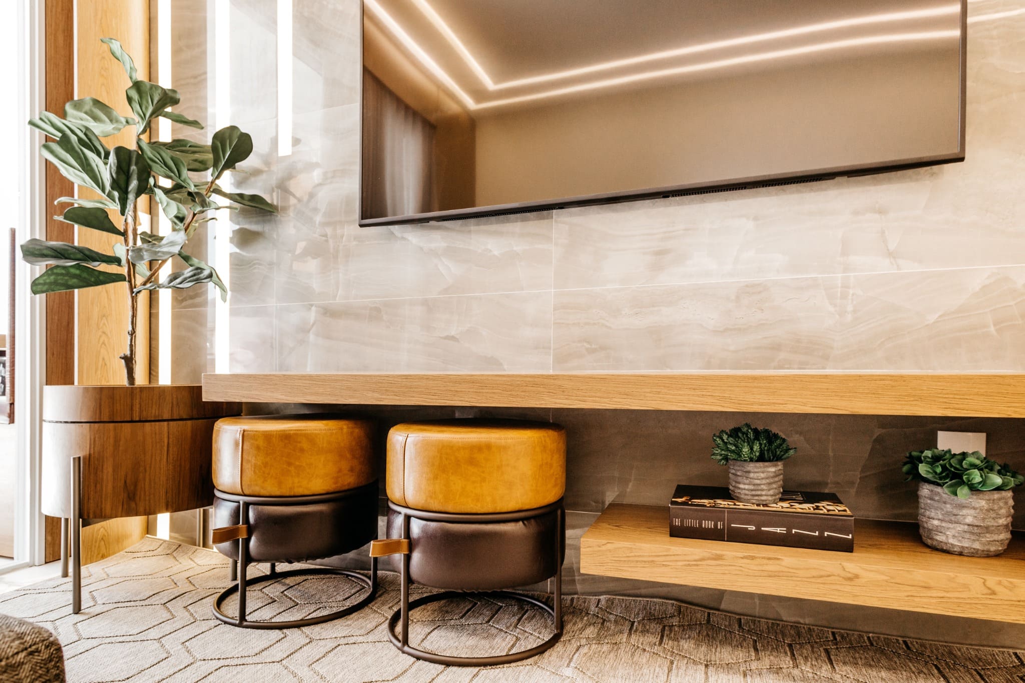 Salon moderne décoré avec des tons chauds, des tabourets en cuir, une plante verte et une ambiance lumineuse naturelle.